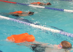 Three children swimming with lifesaving manikins