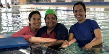Three multicultural women in the pool with pool noodles, smiling