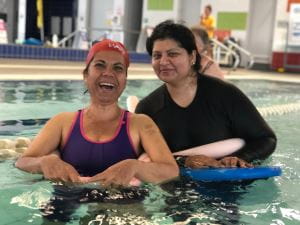 Two multicultural women in the pool with kickboards and smiling