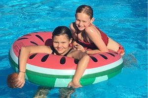 Two girls on a watermelon inflatable in the pool