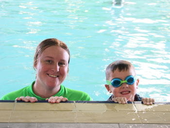 A swim instructor with a little boy by the edge of the pool