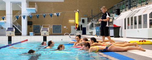 A group of Synchro WA coaches practising rescue skills in the pool watched by a Royal Life Saving trainer