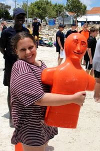 A young girl holding an orange lifesaving manikin