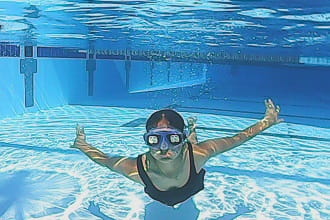 girl wearing blackout goggles at the bottom of a swimming pool