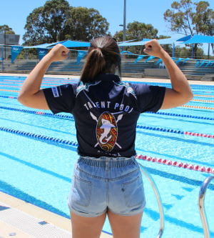 Bree Bugeja standing with back to the camera with arms in muscle pose, showing off her Talent Pool t-shirt