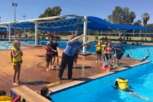 A police officer throwing a rope to a child in the pool wearing a lifejacket
