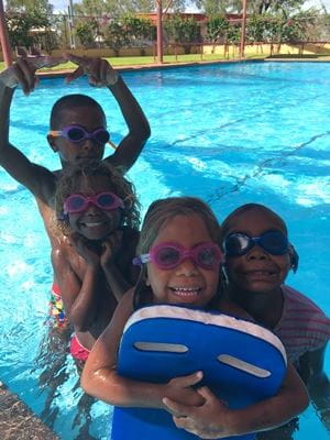 4 aboriginal children wearing goggles and holding kickboards, smiling at the camera while in the pool
