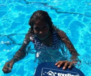 An aboriginal girl in the pool with a kickboard, smiling at the camera