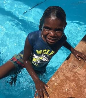 An aboriginal boy in the pool smiling at the camera