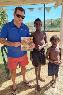 Steve Waterman holding the book Dreaming Soldiers with two Warmun children