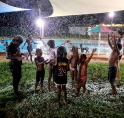 Aboriginal children by the pool at Warmun with snow machine foam falling on them