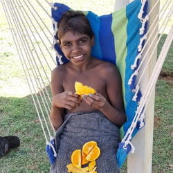 A Warmun boy sitting on a hammock eating oranges