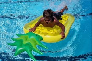 A young Aboriginal boy on a pineapple floatie in the pool