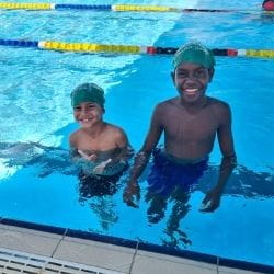 Two Aboriginal boys in the pool wearing Swim For Fruit caps