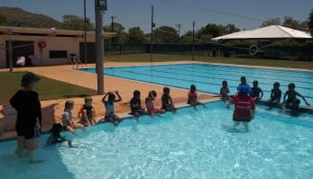children lined up along the edge of the pool with instructor explaining what to do