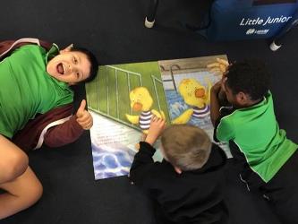 three children laying on the floor reading the Dippy Duck book, one smiling at the camera