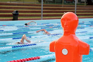 An orange tow manikin by the pool with swimmers swimming in the water behind