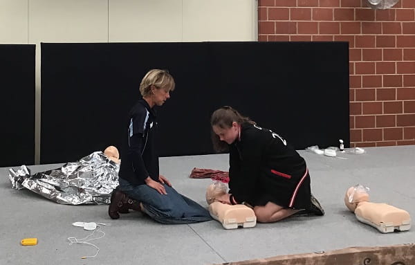first aid trainer teaching primary school girl how to perform CPR