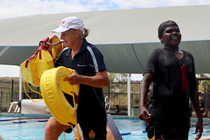 A Royal Life Saving instructor with rescue tubes by the pool with an Aboriginal boy
