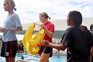 A Royal Life Saving instructor with rescue tubes by the pool with two Aboriginal girls