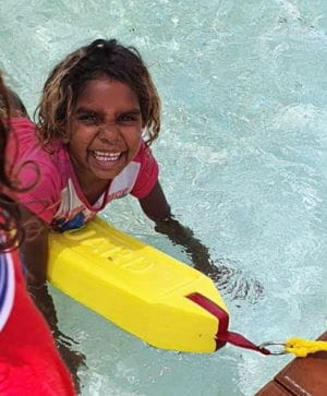 An Aboriginal girl holding a lifeguard rescue tube in the pool at Jigalong