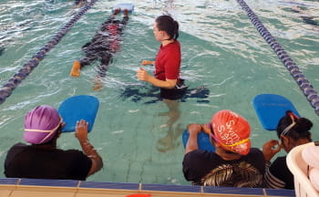 An instructor watching a woman swim a lap with a kickboard
