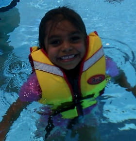 image of an Aboriginal girl wearing a lifejacket in the water and smiling at the camera