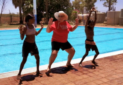 A swim instructor with two aboriginal children dancing by the pool at Yandeyarra