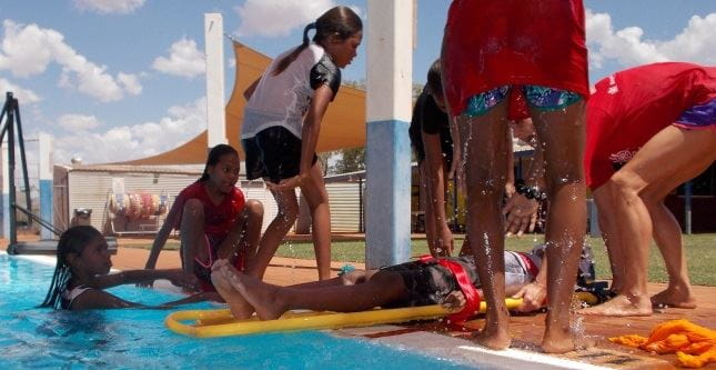 young aboriginal girls practising spinal board techniques by the pool