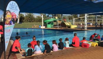 Children sitting along the edge of a pool with their instructor in the water