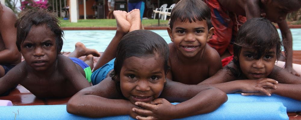 Four aboriginal boys laying by the pool at our remote pools, smiling at the camera