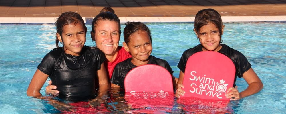 image of 3 aboriginal girls in the pool with their swim instructor and holding Swim and Survive kick boards