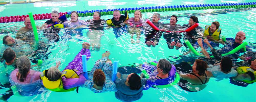 A group of seniors floating on noodles and lifejackets in a pool