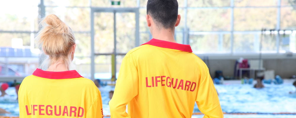 Two pool lifeguards facing the pool watch swimmers