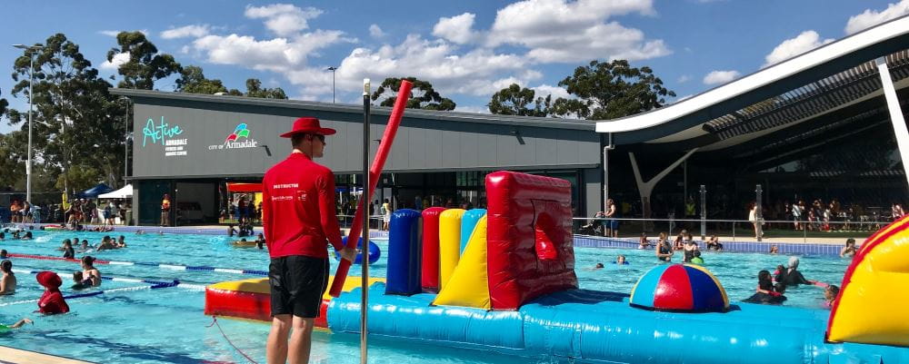 An instructor standing by the pool at Armadale Aquatic Centre with a pool inflatable and people swimming in the background