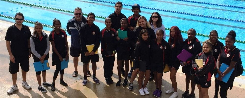 Clontarf College students and teachers stand in front of the outdoor pool at HBF Stadium with Royal Life Saving Society WA staff