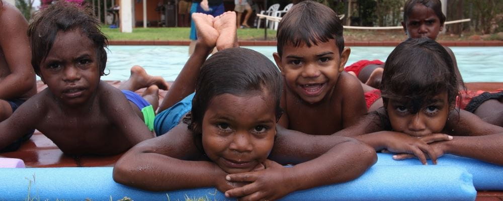 Four aboriginal children leaning on pool noodle beside remote pool