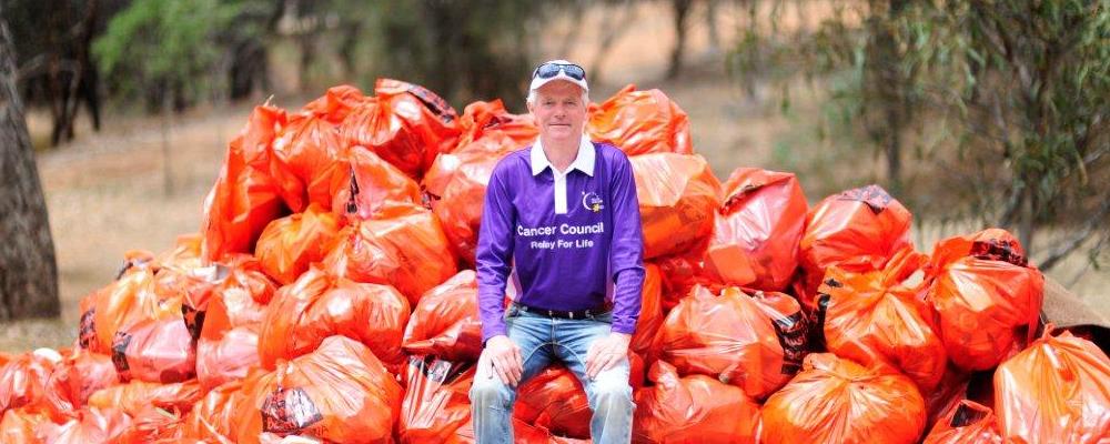 Royal Life Saving Society WA board member Colin Hassell sitting on a stack of full orange rubbish bags in the bush
