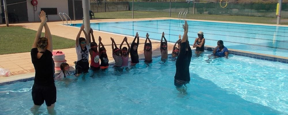 Group of children with two instructors with arms in the air learning diving skills in Warmun remote aboriginal swimming pool