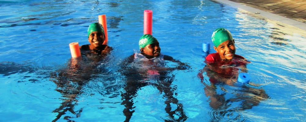 Three Aboriginal girls on pool noodles in Fitzroy Crossing pool