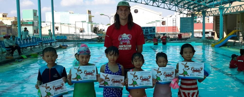 image of swim instructor with six Vietnamese children holding their swimming certificates