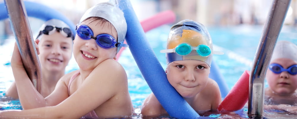 Four children in a swimming pool wearing caps and goggles
