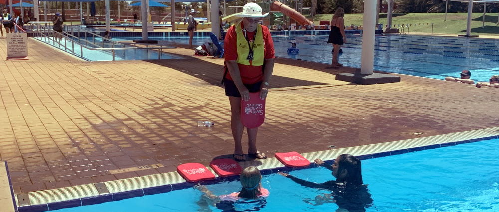 An instructor by the pool with two students in the water