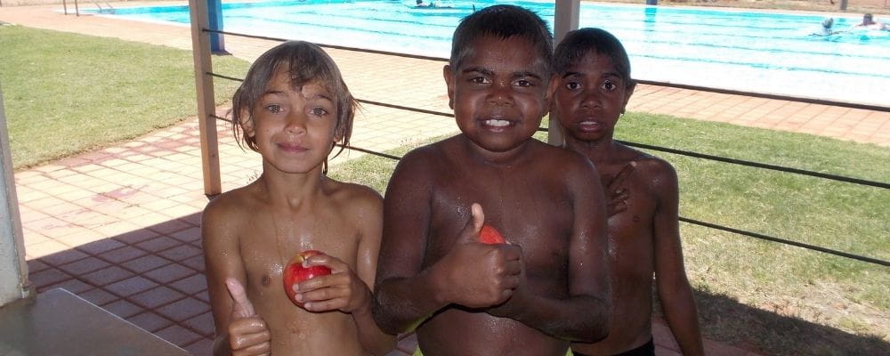 Three Aboriginal boys holding apples by the pool