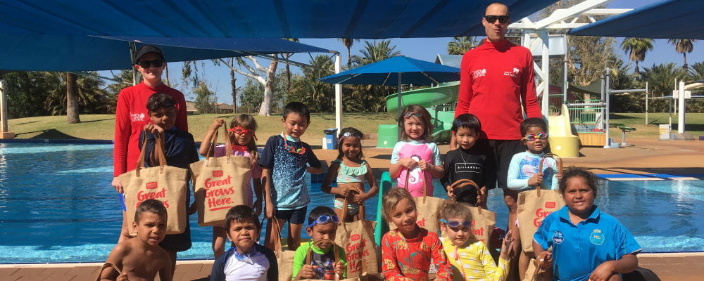 A group of children with two swim instructors standing by the pool at South Hedland holding Uncle Tobys bags
