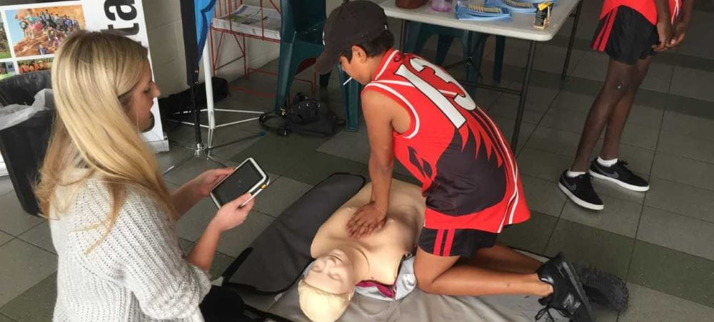 an Aboriginal boy practising CPR on a manikin with a Royal Life Saving staff member timing him