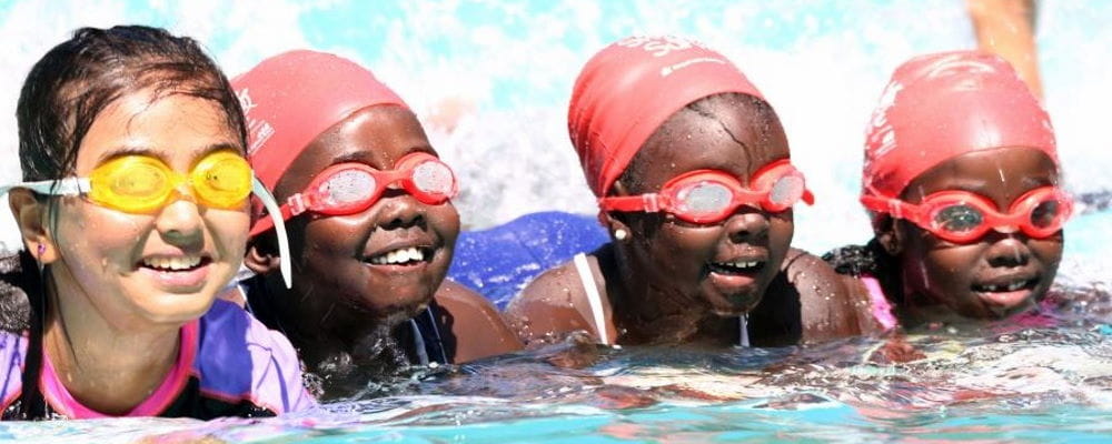 Four multicultural girls wearing goggles and swim caps in the pool