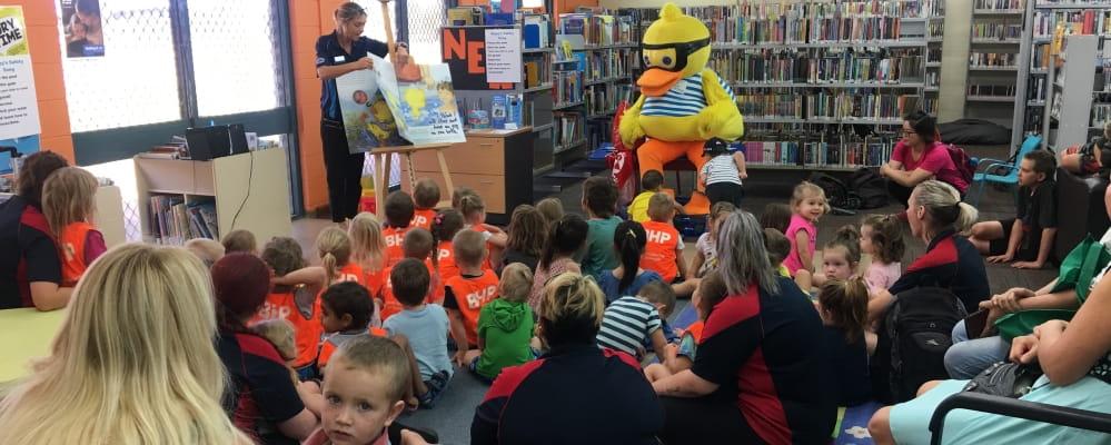 Dippy Duck reads a story book to a large group of young kids in a Port Hedland library