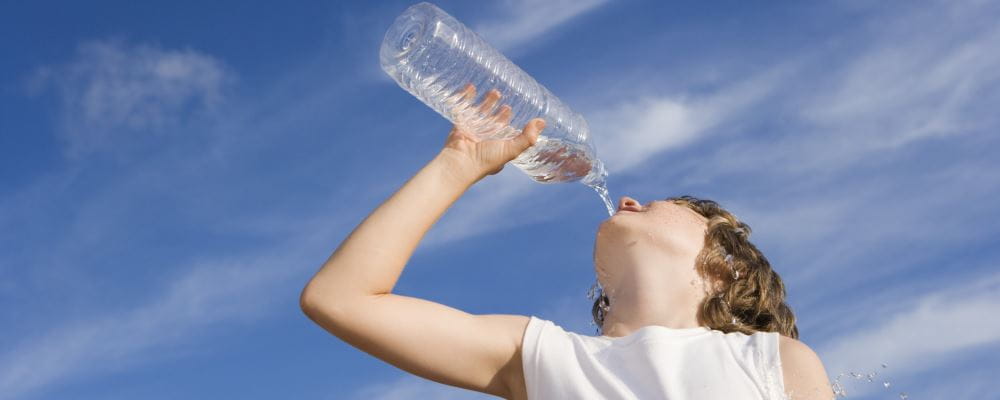 A kid drinks heartily from a bottle of water with bright blue sky behind