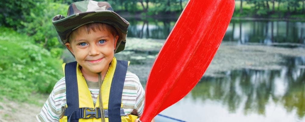 image of small boy wearing lifejacket and holding an oar by the river